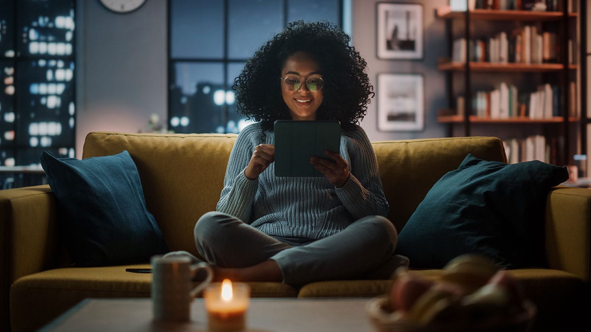 Latina Female Sitting on Couch Reading Tablet at Night