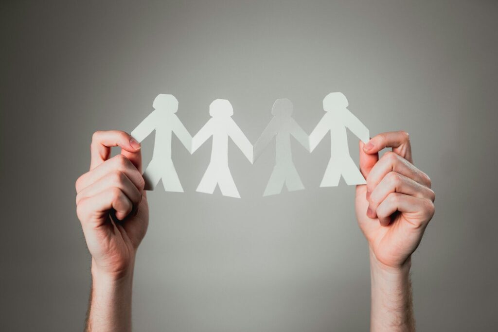 Hands holding a chain of paper dolls, symbolizing unity and connection among people.
