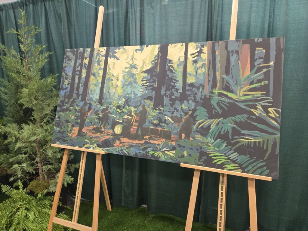 WordCamp's community painting rests on two easels. The canvas depicts a forest scene with tall trees and dense foliage, surrounded by actual potted plants. A green curtain hangs in the background.