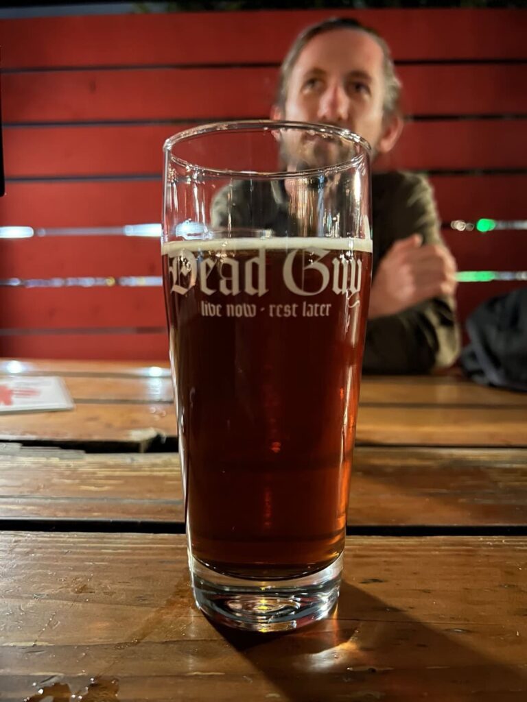 A glass of amber-colored pumpkin beer from Rogue Brewery sits on a wooden table with Max in the background.