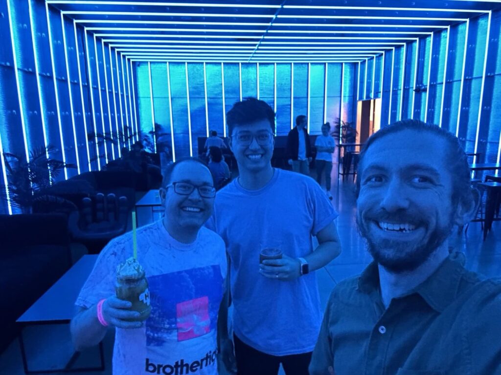 The Razorfrog team smiling in a neon-lit room with blue lighting. The setting includes modern decor and geometric lighting patterns on the ceiling and walls.
