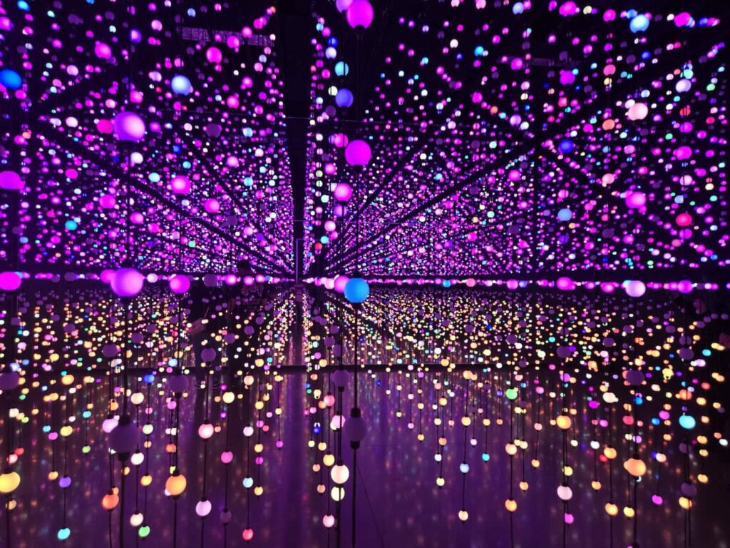 A mesmerizing installation of hanging, multicolored LED orbs, creating a dazzling pattern of lights in hues of pink, purple, blue, and orange. The lights appear to extend infinitely, giving an immersive, otherworldly ambiance.